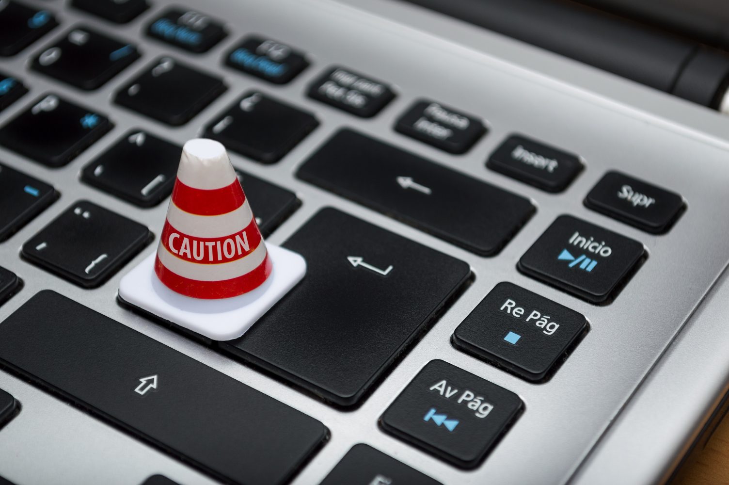 Laptop keyboard with a miniature traffic cone placed on the enter key reading Caution