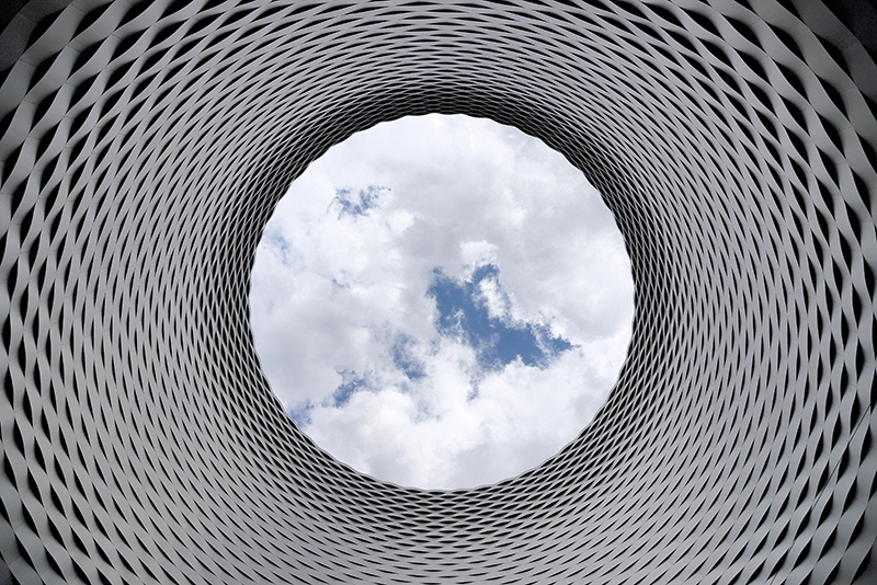 Ground-level view looking up at the clouds through a large abstract modern piece of sculpture or architecture