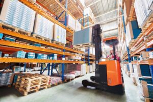 Forklift operator using a forklift to load a pallet of goods onto a warehouse shelf