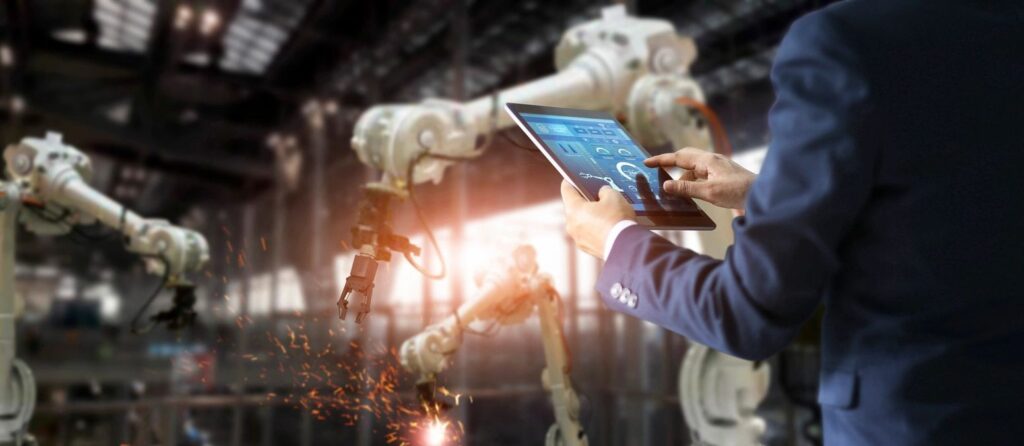 Business executive uses a dashboard on their tablet as robotic arms work in a factory in the background