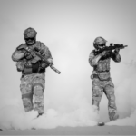 Two modern soldiers holding firearms wearing tactical gear surrounded by smoke from nearby cannisters